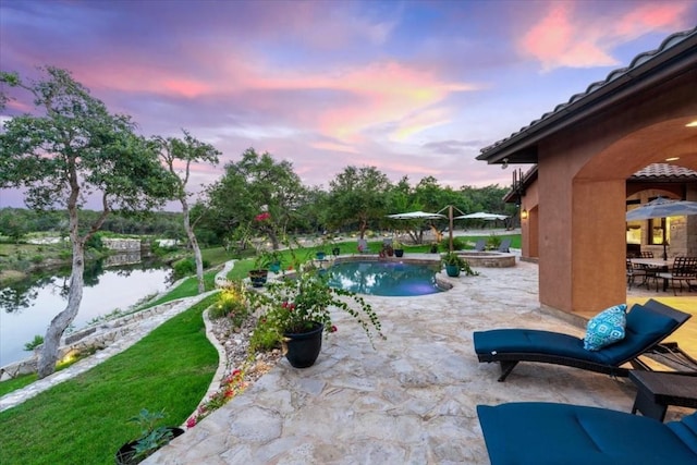 pool at dusk featuring a patio and a water view