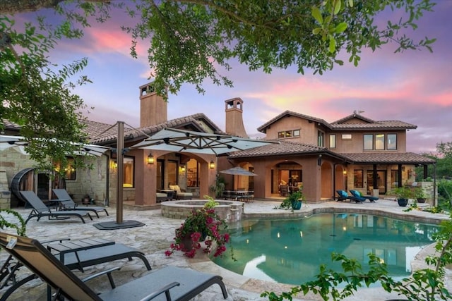 back house at dusk with a pool with hot tub and a patio area