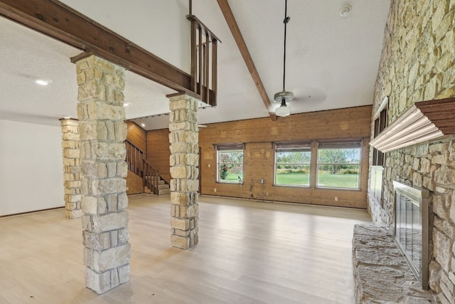 unfurnished living room featuring lofted ceiling with beams, hardwood / wood-style floors, a stone fireplace, a textured ceiling, and ornate columns