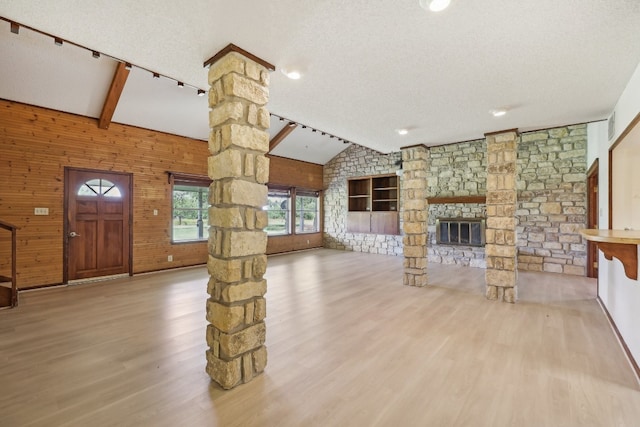 unfurnished living room featuring wooden walls, a textured ceiling, a stone fireplace, wood-type flooring, and lofted ceiling with beams