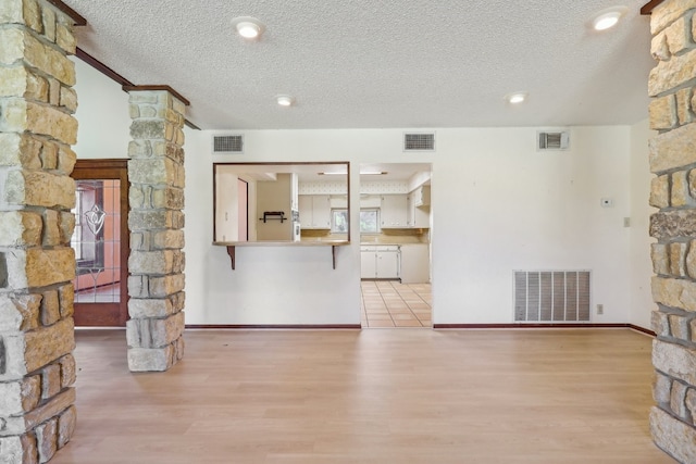 unfurnished living room featuring a textured ceiling, light hardwood / wood-style flooring, and ornate columns