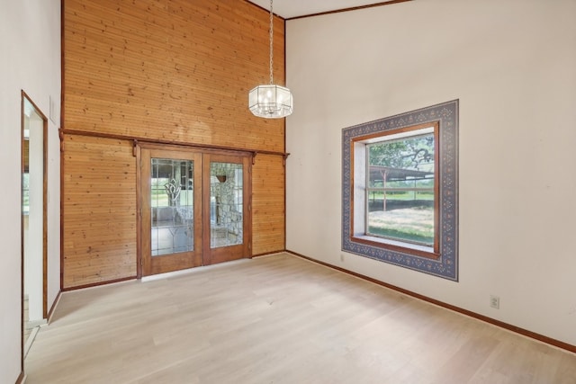 empty room featuring a high ceiling, wood walls, french doors, and hardwood / wood-style floors