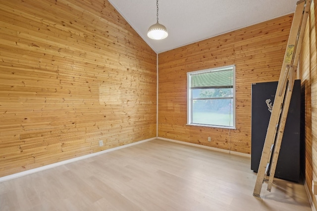 unfurnished room with hardwood / wood-style floors, wood walls, and vaulted ceiling