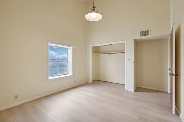 unfurnished bedroom with a high ceiling, light hardwood / wood-style flooring, and a closet