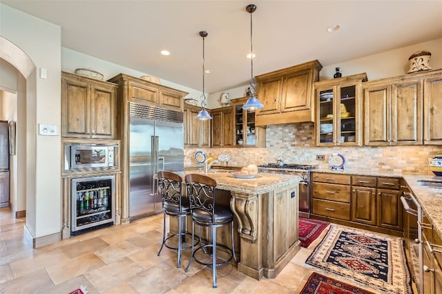 kitchen with built in appliances, backsplash, wine cooler, a center island, and light stone countertops