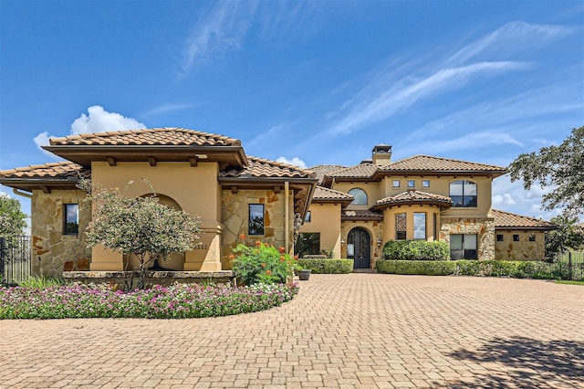 mediterranean / spanish-style house with stone siding, a chimney, and a tile roof