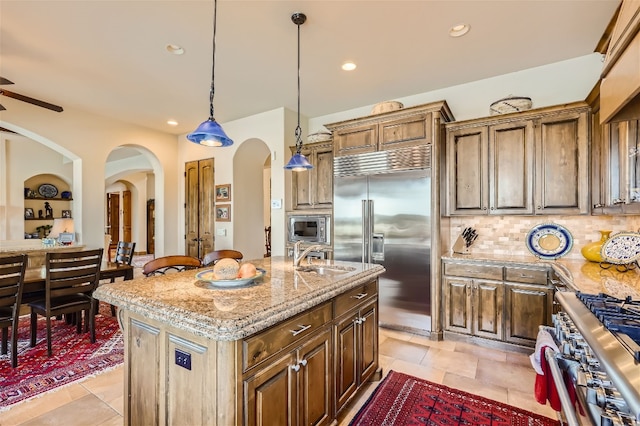 kitchen with built in appliances, light tile patterned floors, decorative backsplash, and an island with sink