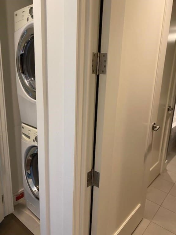 laundry area with light tile patterned floors and stacked washer / dryer