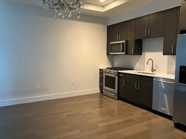 kitchen with light wood-type flooring, stainless steel appliances, a raised ceiling, sink, and an inviting chandelier