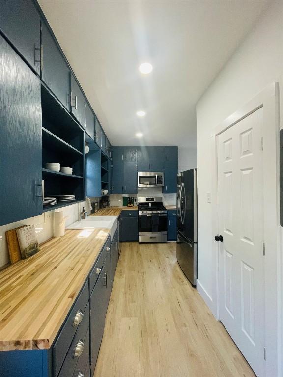 kitchen with appliances with stainless steel finishes, butcher block counters, sink, and light hardwood / wood-style flooring