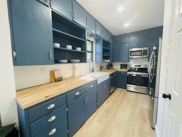 kitchen with appliances with stainless steel finishes, blue cabinets, tasteful backsplash, butcher block counters, and light wood-type flooring