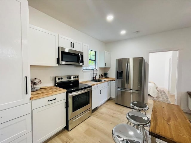 kitchen with white cabinetry, wood counters, stainless steel appliances, and sink