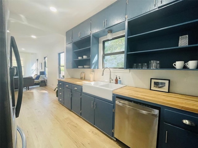 kitchen with sink, light hardwood / wood-style flooring, butcher block counters, black refrigerator, and stainless steel dishwasher