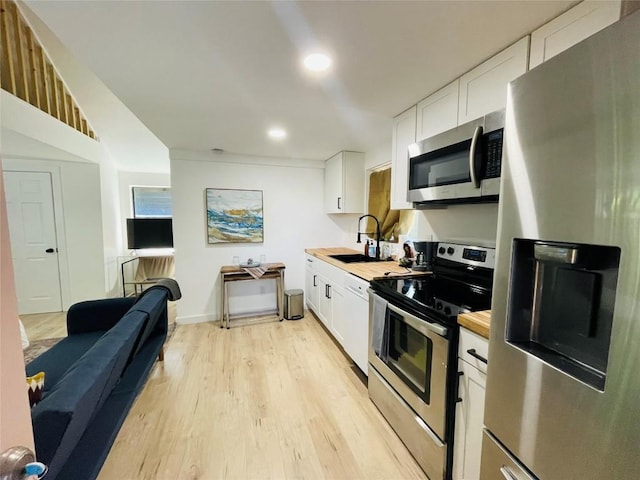 kitchen with appliances with stainless steel finishes, wood counters, sink, white cabinets, and light hardwood / wood-style floors