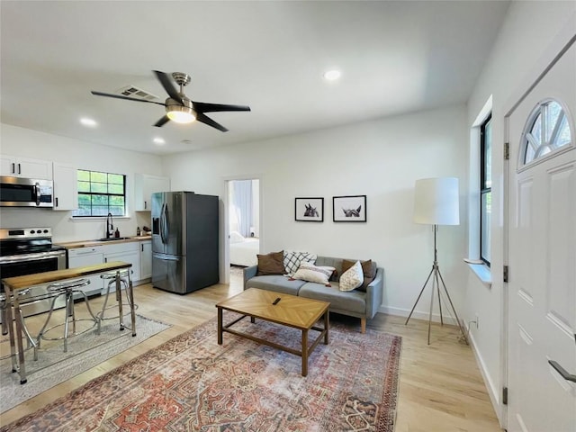 living room with ceiling fan, sink, and light wood-type flooring