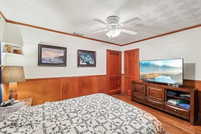 bedroom featuring ceiling fan, light wood-type flooring, wood walls, and ornamental molding