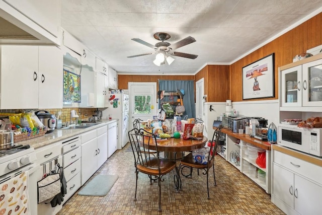 kitchen with ceiling fan, sink, white appliances, wooden walls, and white cabinets