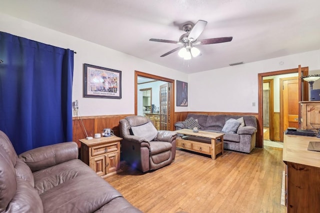 living room with ceiling fan, wood walls, and light hardwood / wood-style flooring