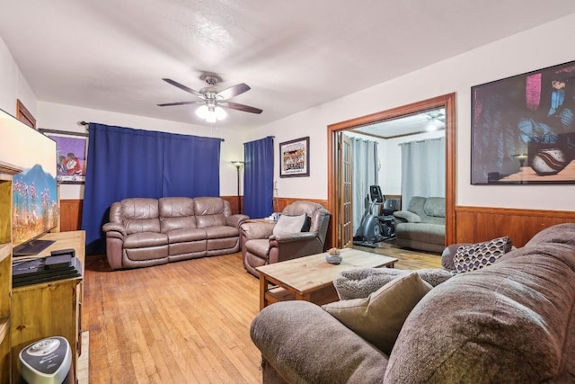 living room with light hardwood / wood-style floors, ceiling fan, and wooden walls