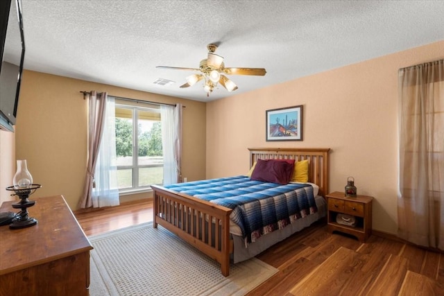 bedroom with a textured ceiling, wood finished floors, visible vents, and a ceiling fan