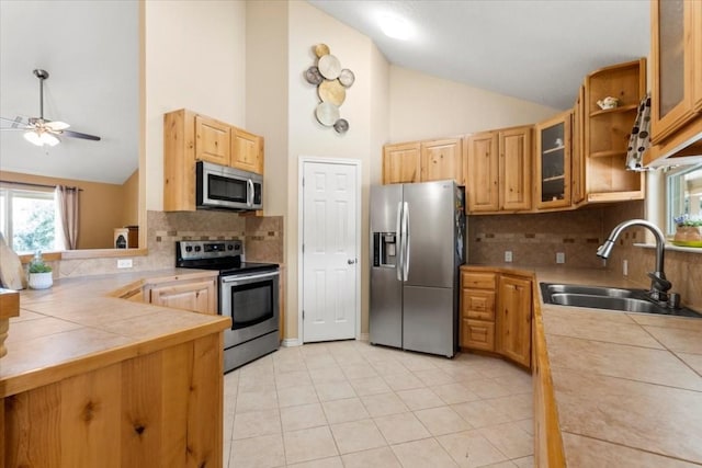 kitchen with stainless steel appliances, a sink, tile counters, open shelves, and glass insert cabinets