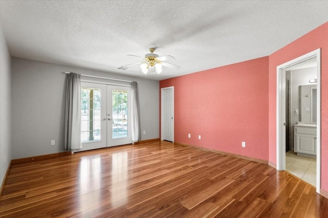 empty room with baseboards, ceiling fan, wood finished floors, a textured ceiling, and french doors