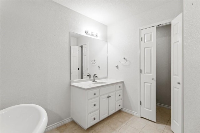 bathroom with a closet, a freestanding bath, vanity, baseboards, and tile patterned floors