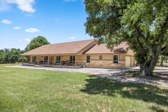 rear view of property with driveway, a garage, stone siding, a yard, and stucco siding