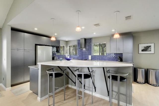 kitchen with tasteful backsplash, wall chimney range hood, light hardwood / wood-style floors, pendant lighting, and white refrigerator