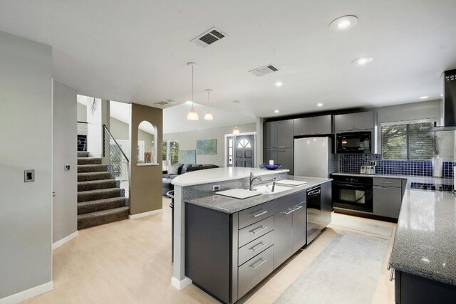 kitchen featuring black appliances, hanging light fixtures, a center island with sink, light hardwood / wood-style flooring, and backsplash