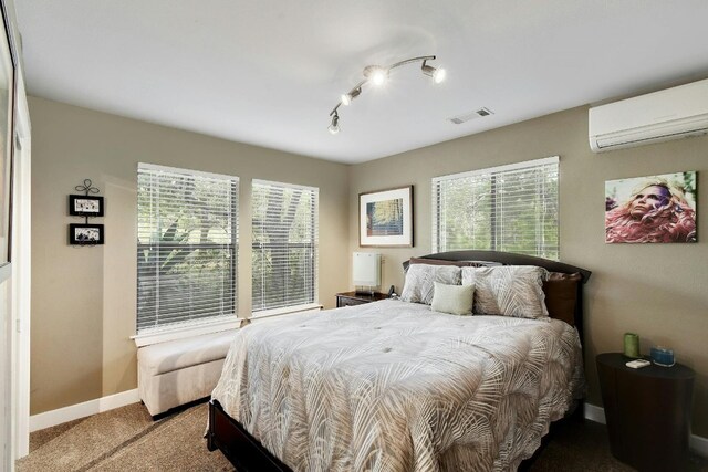 carpeted bedroom featuring rail lighting, a wall mounted AC, and multiple windows