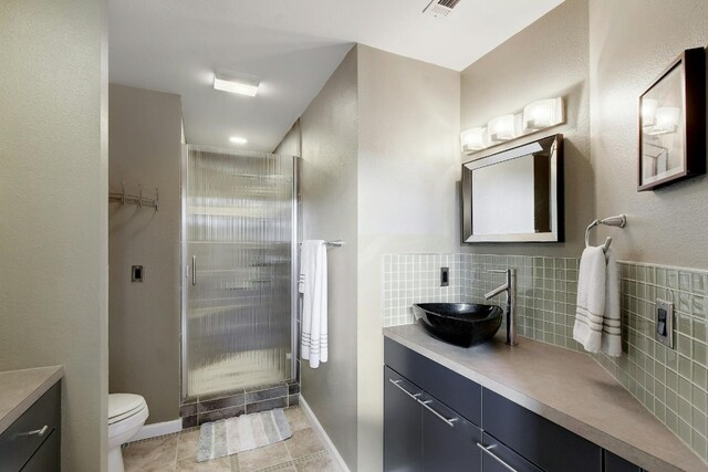 bathroom featuring a shower with shower door, vanity, decorative backsplash, and toilet