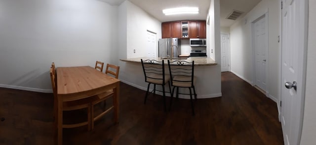 kitchen featuring light stone countertops, dark hardwood / wood-style flooring, kitchen peninsula, a breakfast bar area, and appliances with stainless steel finishes