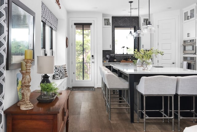 kitchen featuring white cabinetry, decorative light fixtures, a kitchen breakfast bar, and a wealth of natural light