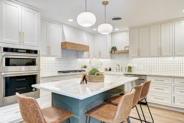 kitchen with white cabinets, custom exhaust hood, stainless steel appliances, and hanging light fixtures