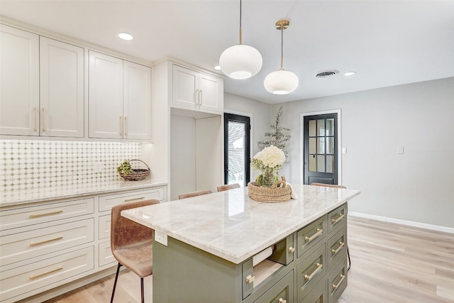 kitchen with light stone countertops, pendant lighting, white cabinets, light hardwood / wood-style floors, and a kitchen island