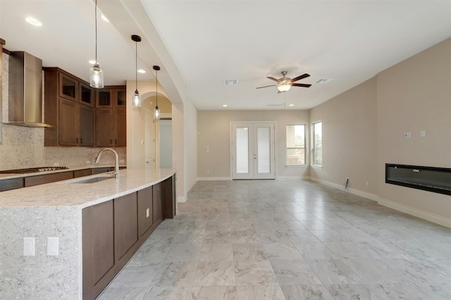 kitchen featuring tasteful backsplash, wall chimney range hood, sink, pendant lighting, and ceiling fan