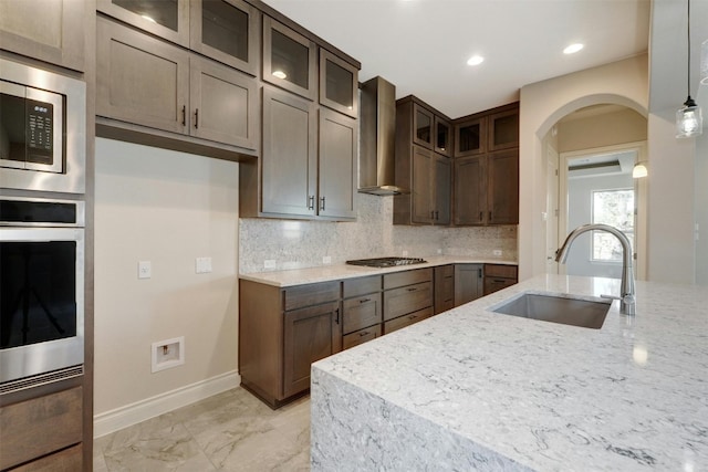 kitchen featuring appliances with stainless steel finishes, tasteful backsplash, wall chimney range hood, sink, and light tile patterned floors