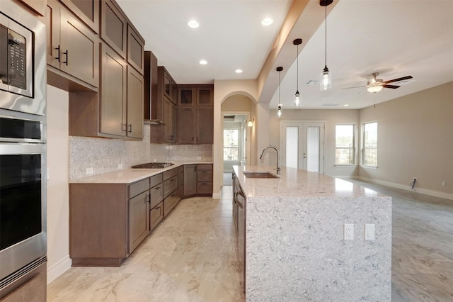 kitchen featuring appliances with stainless steel finishes, wall chimney range hood, sink, backsplash, and light tile patterned floors