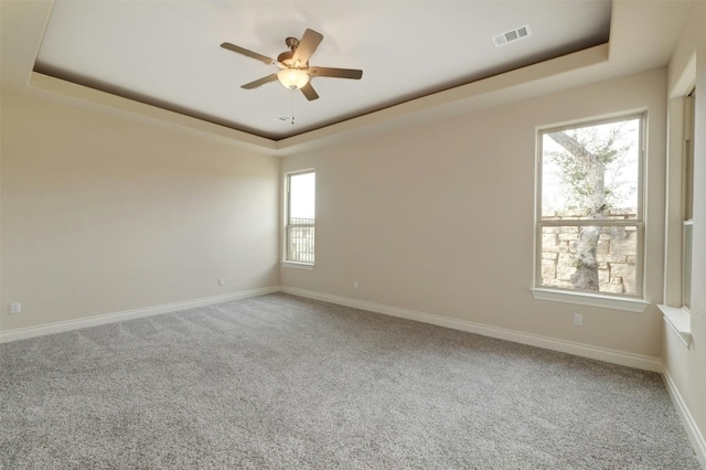 carpeted spare room featuring ceiling fan, a tray ceiling, and a wealth of natural light