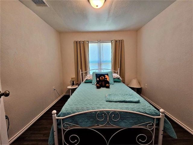 bedroom featuring visible vents, dark wood-type flooring, baseboards, and a textured wall