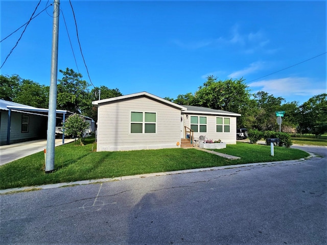 manufactured / mobile home with driveway, a carport, a front lawn, and entry steps