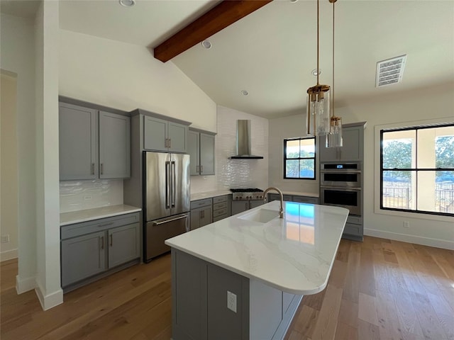 kitchen featuring stainless steel appliances, plenty of natural light, a kitchen island with sink, and wall chimney range hood