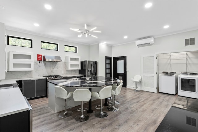 kitchen featuring washer and clothes dryer, a wall mounted air conditioner, backsplash, appliances with stainless steel finishes, and a kitchen island