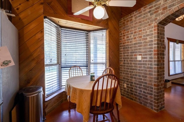 dining area featuring ceiling fan, wood walls, brick wall, and vaulted ceiling