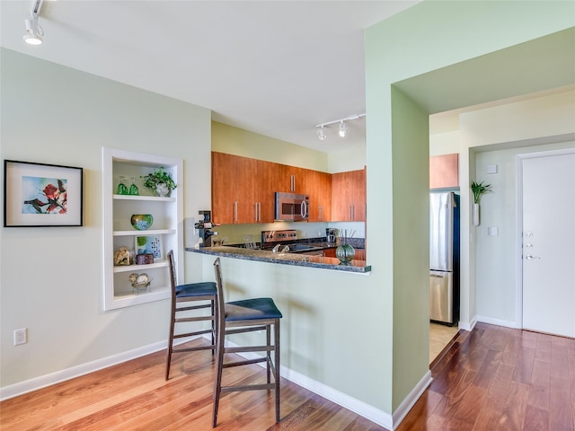 kitchen featuring stainless steel appliances, light hardwood / wood-style floors, kitchen peninsula, dark stone counters, and built in shelves