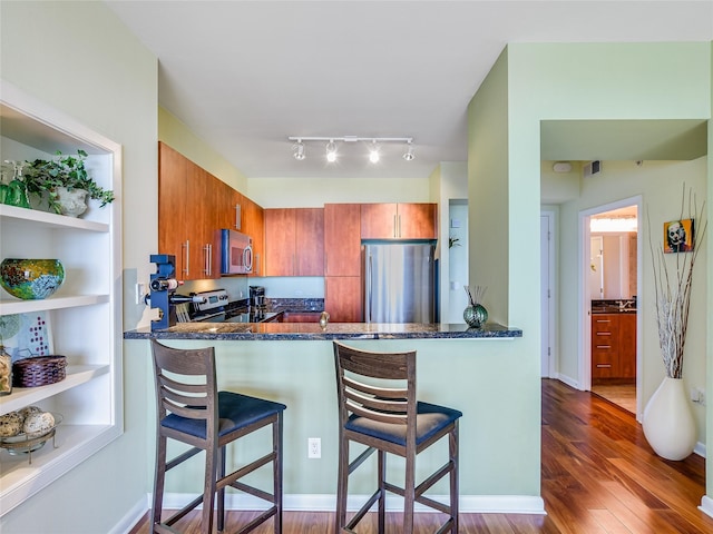 kitchen featuring kitchen peninsula, dark hardwood / wood-style floors, stainless steel appliances, a kitchen bar, and dark stone countertops