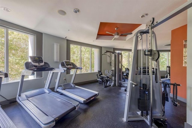 exercise room with ceiling fan, a wealth of natural light, and a tray ceiling