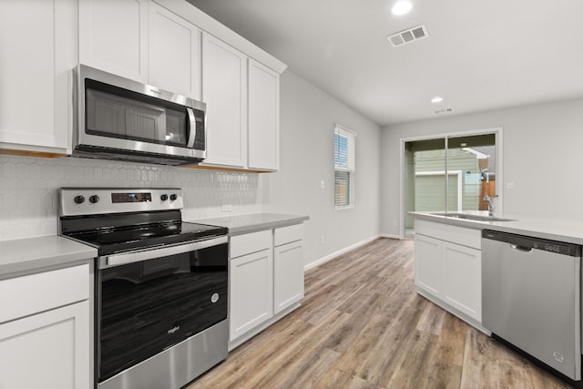 kitchen featuring tasteful backsplash, appliances with stainless steel finishes, light wood-type flooring, and white cabinets