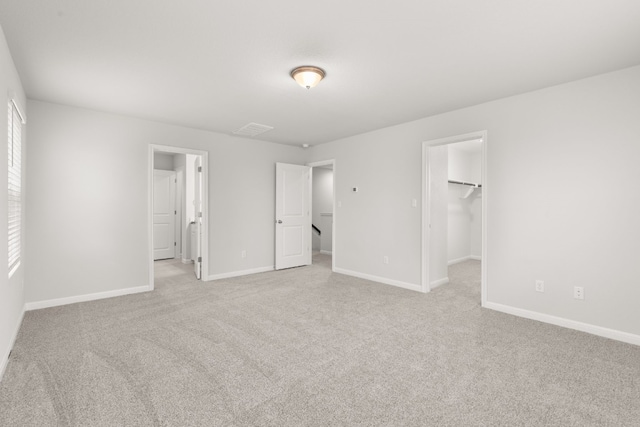 unfurnished bedroom featuring a spacious closet, light colored carpet, and a closet